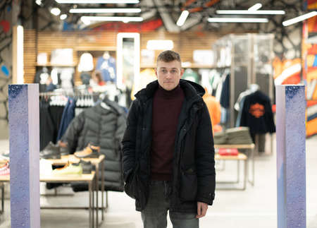 Young man in a jacket in a shopping center leaves the store through the turnstileの写真素材