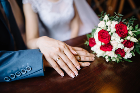bride and groom in a cafe. wedding bouquet of roses on a wooden table in a restaurant, bride and groom hold each others hands. Wedding rings. Loving couple in a cafe. hot tea for loversの写真素材