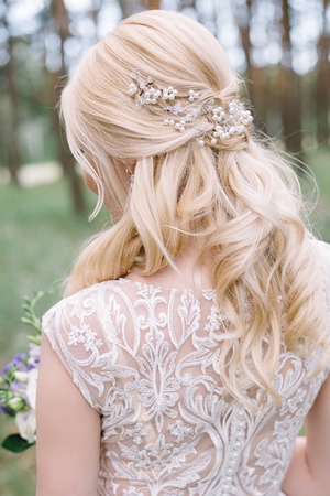 Portrait of lovely young bride with beautiful blond hair and curled hairstyle turned away on green...