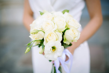 Beautiful fresh wedding bouquet of roses and other flowers in beige light colors in the hands of the bride. Close-up shot, soft focus, background blur.の写真素材