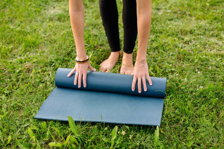 Close-up of young woman with exercise mat preparing for sports training outdoors. A strong successful sports coach, practices yoga and relaxes in the evening on the street. High quality shot.の写真素材