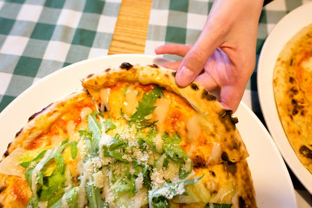 Female hands taking slices of authentic Italian caesar stone oven pizza with arugula, sauce, grilled chicken, herbs and spicy parmesan cheese. High quality photo.の写真素材