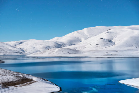 Beautiful winter landscape. Panoramic view on the lake and mountains peaks snow-covered at the starry moon night.の写真素材