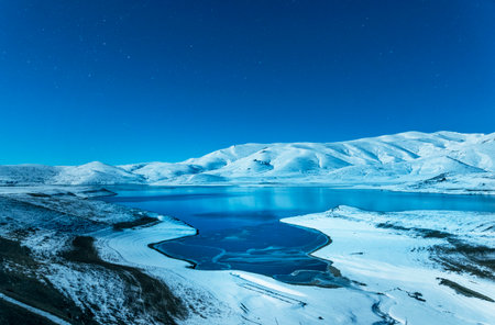 Beautiful winter landscape. Panoramic view on the lake and mountains peaks snow-covered at the starry moon night.の写真素材