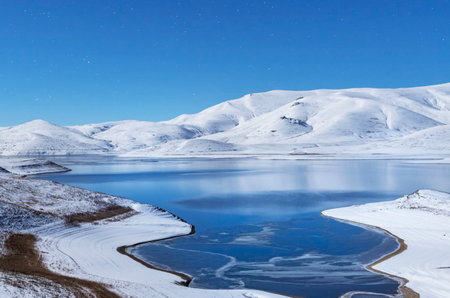 Beautiful winter landscape. Panoramic view on the lake and mountains peaks snow-covered at the starry moon night.の写真素材