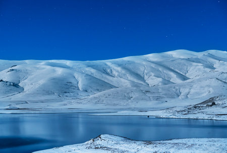 Beautiful winter landscape. Panoramic view on the lake and mountains peaks snow-covered at the starry moon night.の写真素材