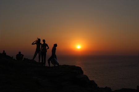 Silhouettes of five people on mountainside on a background of sunset and seaの写真素材