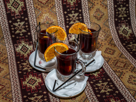Three high glasses of mulled wine with spicy orange slices on saucersの写真素材