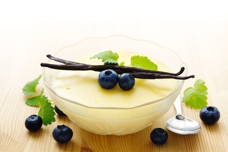 Bowl of homemade vanilla pudding decorated with vanilla beans and blueberries