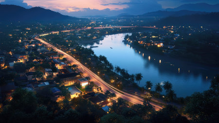 A stunning evening view of a tranquil riverfront in Thailand, showcasing illuminated homes and lush palm trees under a vibrant twilight sky. Perfect for showcasing natural beauty and serenity.の素材