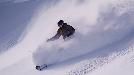A snowboarder carving down a snowy slope, kicking up fresh powder as they make their way down.の素材