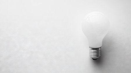 Flat lay of a light bulb with a clean, white surface, providing plenty of room for text or product placement on one side.の素材