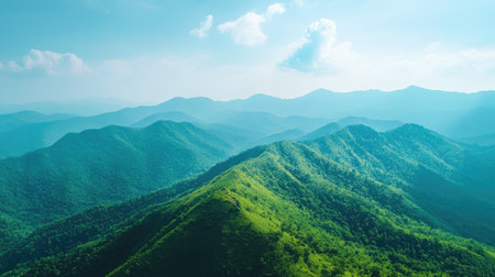Top view of a lush green mountain range, with a large expanse of blue sky for copy space, ideal for outdoor adventure or nature advertisements.の素材