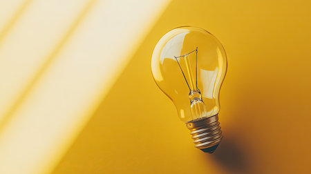 Top view of a light bulb on a bright surface with a large open area beside it for copy or branding.の素材