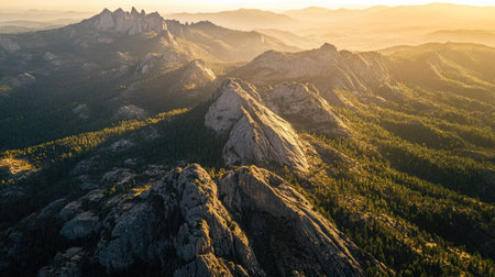 Top view of a rugged mountain range with jagged peaks, casting long shadows over a forested valley at sunriseの素材