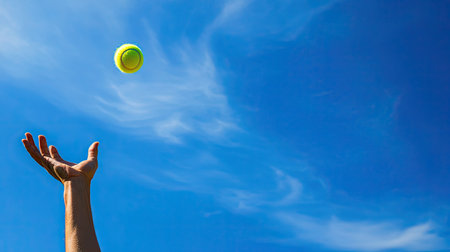 Tennis player tossing the ball for a serve, with ample sky space for copy.の素材