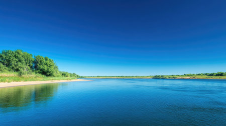 A tranquil river flowing past a sandy beach with clear blue sky above, providing plenty of space for text placement.の素材