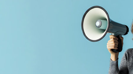 Close-up of a woman holding a megaphone speaker against a clear blue background, perfect for advertisements or announcements with space for additional text.の素材