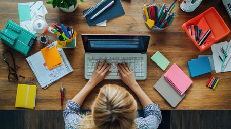 Top view of a businesswoman's hands typing on a keyboard with office supplies nearby.の素材