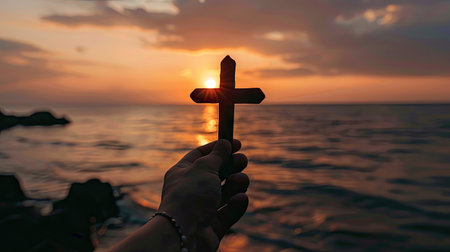 Human hand holding a cross in silhouette, with a breathtaking sunrise creating a serene and inspiring backdrop with this inviting photo.の素材