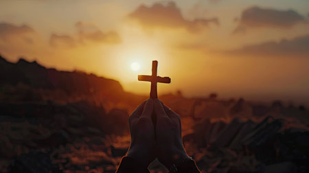 Human hand holding a cross in silhouette, framed by the warm hues of a sunrise, representing faith and tranquility with this inviting photo.の素材