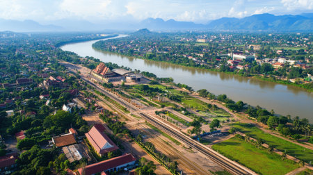 A stunning aerial view capturing the Lao China Railway Station amidst a vibrant landscape with a river, mountains, and lush greenery. Ideal for travel and infrastructure themes.の素材