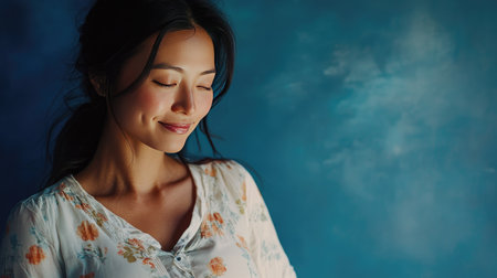 A beautiful close-up of a pregnant Asian woman embracing her belly, against a deep blue backdrop, emphasizing the connection between health, motherhood,の素材
