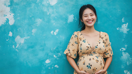 A cheerful portrait of a pregnant Asian woman with a radiant smile, surrounded by a blue background, conveying happiness and positivity during pregnancy.の素材
