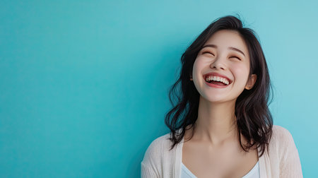 A joyful portrait of a pregnant Asian woman laughing, with a bright blue background providing a cheerful setting, perfect for maternity and family-related themes.の素材