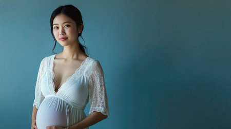 An elegant portrait of a pregnant Asian woman standing confidently, set against a calm blue background, perfect for celebrating motherhoodの素材