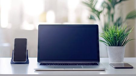 Modern office scene with a blue MacBook, smartphone, and plant on a white desk. Clean lines and a pop of color create a fresh, tech-savvy environment.の素材
