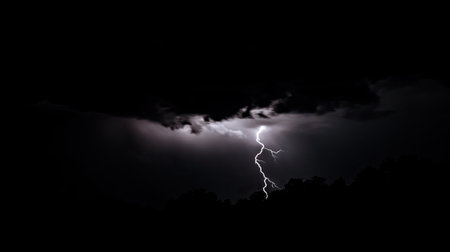 Lightning bolt illuminating a pitch-black night sky, the sudden flash revealing the storm's intensity.の素材