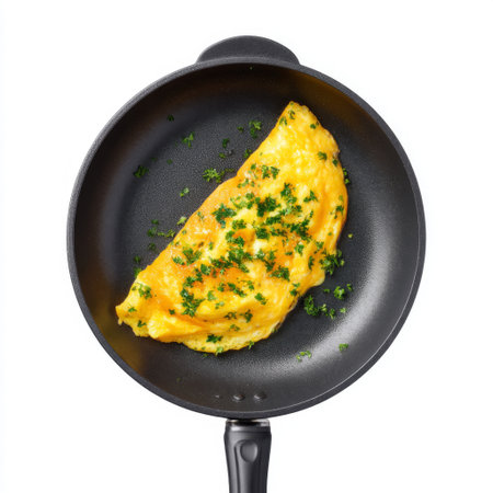 This image showcases a delicious and fluffy omelet garnished with fresh herbs, presented in a black nonstick frying pan, perfect for breakfast or brunch.の素材
