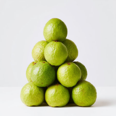A vibrant arrangement of fresh green citrus fruits stacked in a pyramid shape against a clean white background, symbolizing health and nutrition.の素材