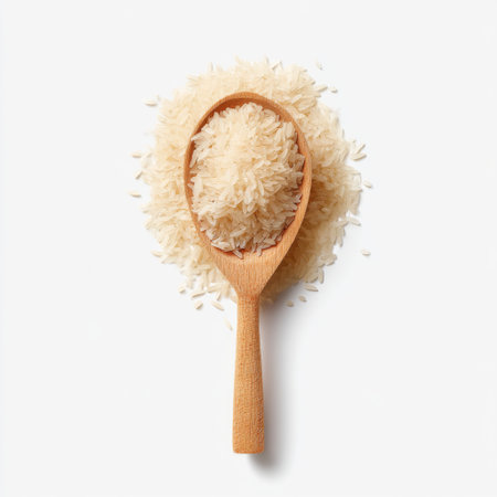 A wooden spoon filled with uncooked white rice rests on a beige background with scattered grains around. Ideal for culinary themes and food presentations.の素材