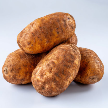 A close-up view of fresh raw sweet potatoes stacked on a clean surface, showcasing their earthy brown skins and nutritious appeal for healthy meals.の素材