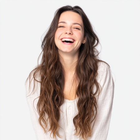 A joyful young woman with long hair smiles brightly against a soft light background, radiating happiness and positivity in a natural and carefree manner.の素材