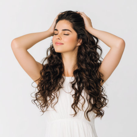 A beautiful young woman with long curly hair stands gracefully in bright studio light, showcasing her natural beauty and joyful personality.の素材