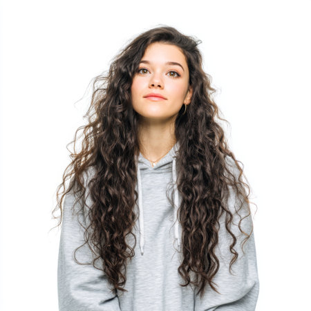 A young woman with long curly hair poses thoughtfully in a casual grey hoodie. Her natural beauty shines through with a subtle smile, creating a relaxed atmosphere.の素材