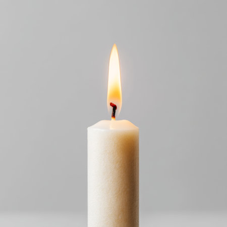 A serene white candle with a bright flickering flame stands against a minimalist gray backdrop, evoking a sense of peace and tranquility. Perfect for relaxation or decor.の素材