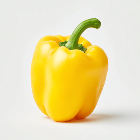 A single yellow bell pepper resting against a clean white background, showcasing its glossy skin and natural curves, perfect for food and health visuals.の素材