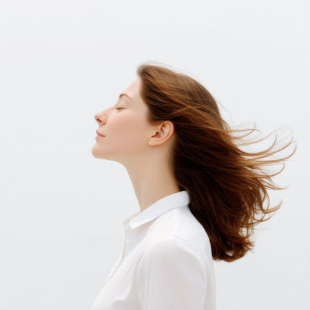 A serene young woman with flowing hair stands in profile, enjoying a gentle breeze. Her calm expression embodies tranquility and beauty against a minimalist background.の素材