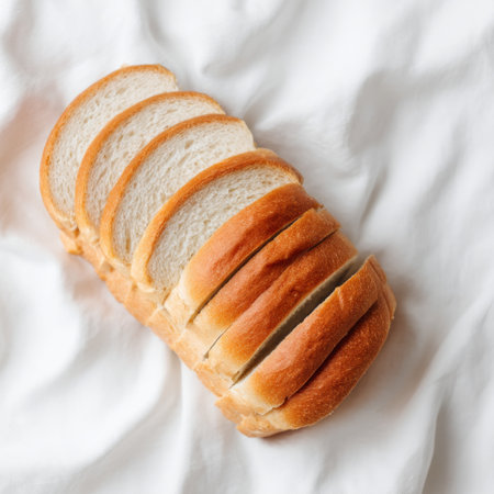 A freshly sliced loaf of bread rests on a soft white textile background, highlighting its texture and inviting warmth, ideal for food photography.の素材
