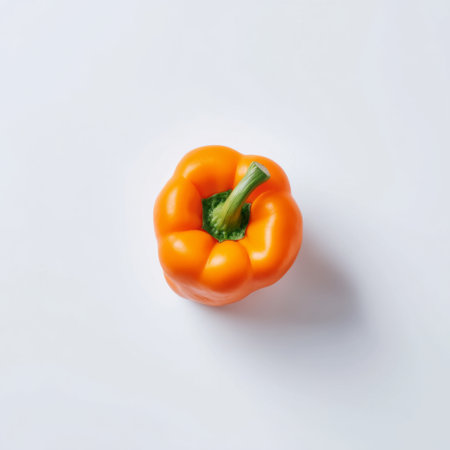 A single bright orange bell pepper rests on a clean white background, showcasing its smooth texture and vibrant color, perfect for cooking or healthy eating ideas.の素材
