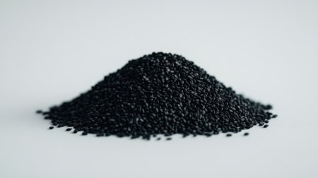 A close-up view of a pile of black sesame seeds on a light background. These seeds are known for their nutty flavor and health benefits. Ideal for culinary use.の素材