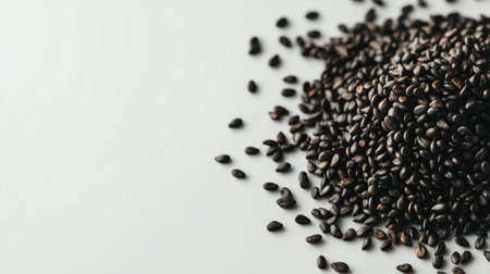 A close-up view of black sesame seeds scattered on a white background, perfect for recipes or health-related concepts. Ideal for food photography.の素材