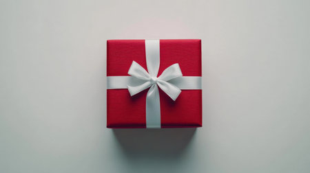 A classic red gift box with a white satin ribbon, set against a white background, conveying simplicity and elegance for holiday imagery.の素材