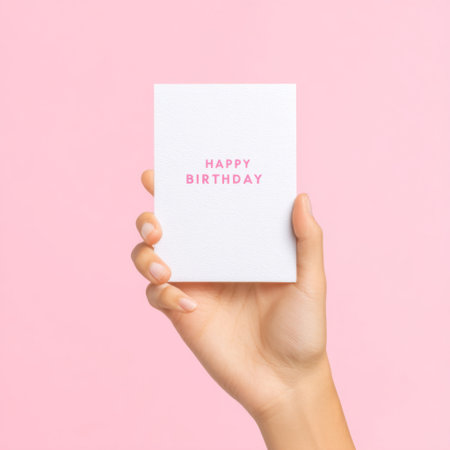 A hand holding a cheerful birthday card featuring pink text on a soft pink background, perfect for celebrating special moments and sharing joy.の素材