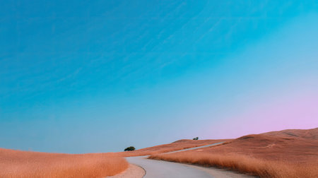 A serene winding road stretches through golden grass hills under a clear blue sky, epitomizing the beauty of nature and inviting peaceful travel explorations.の素材
