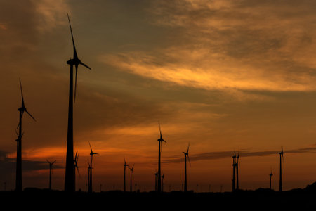 Silhouettes of wind turbines producing renewable energy at sunsetの写真素材
